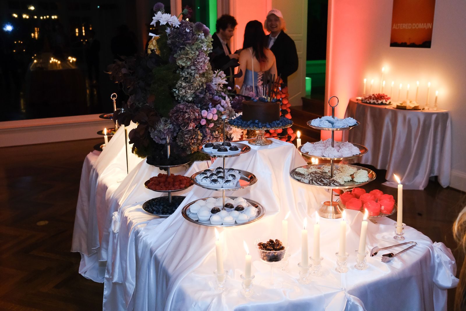 A candlelit dessert table layered with tiered stands and flowers