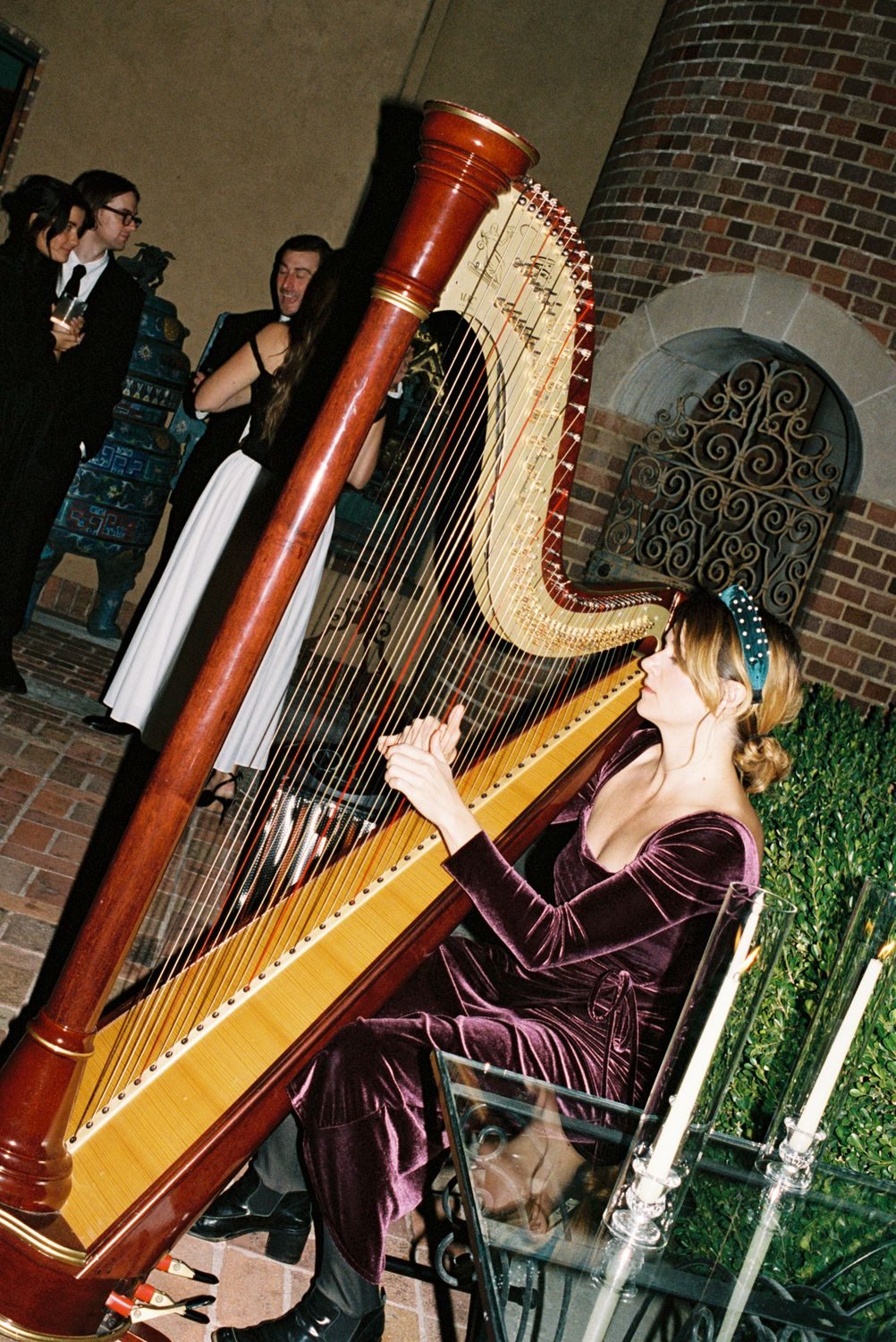 A harpist in purple velvet plays in a candlelit courtyard