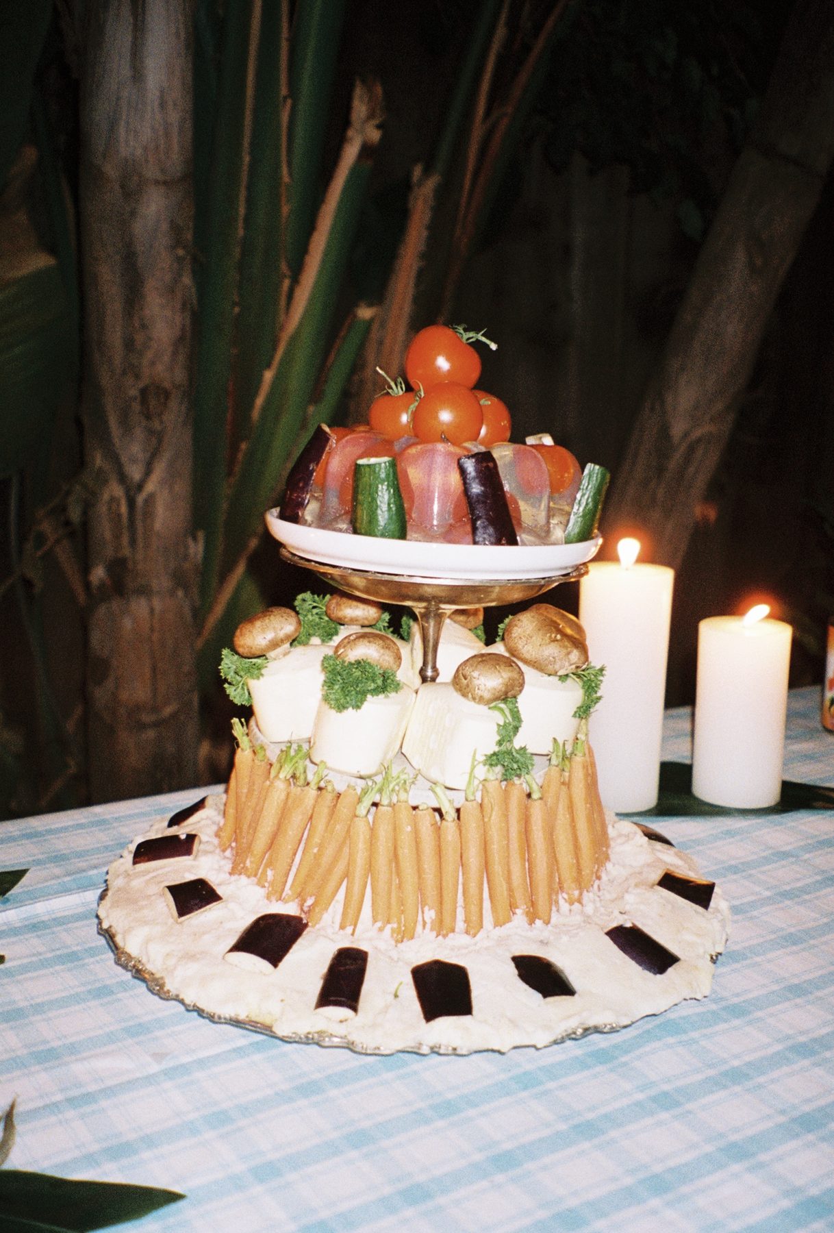 A sculptural produce centerpiece of tomatoes, eggplant and carrots by candlelight