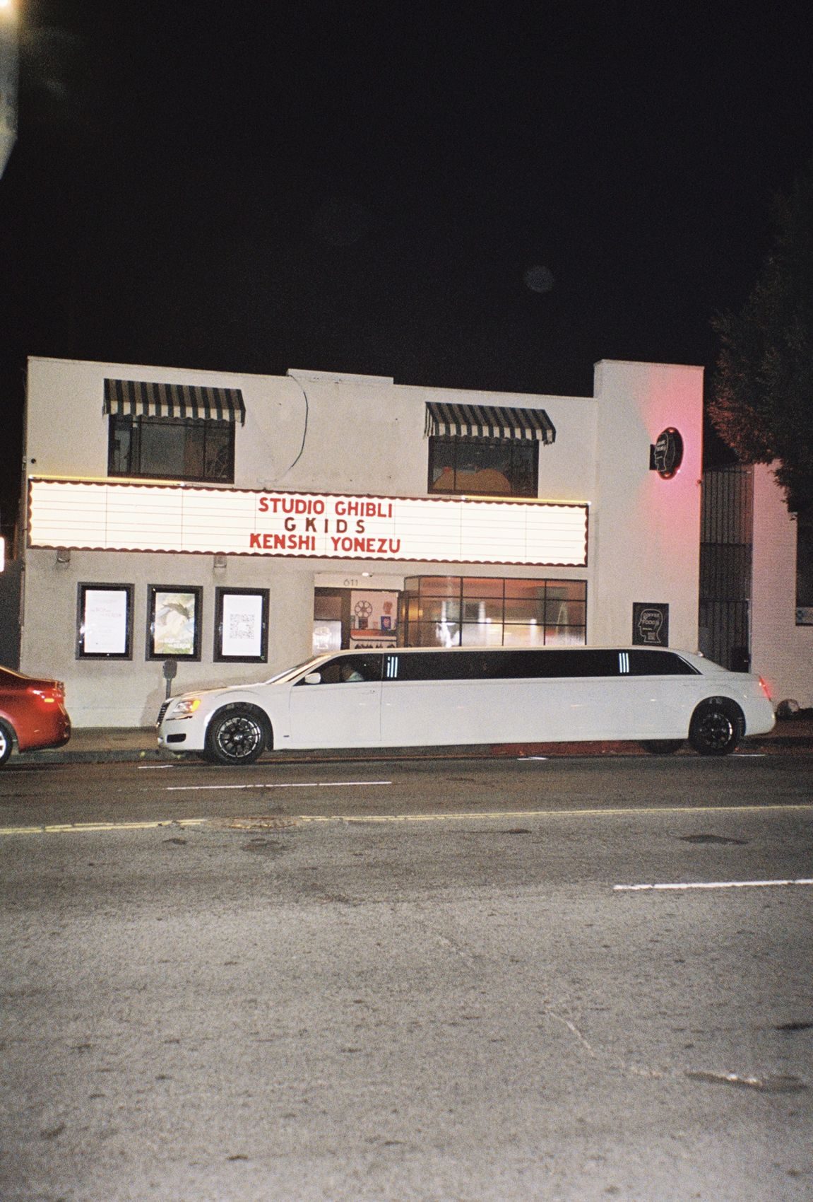 A white stretch limousine outside the lit theater marquee at night