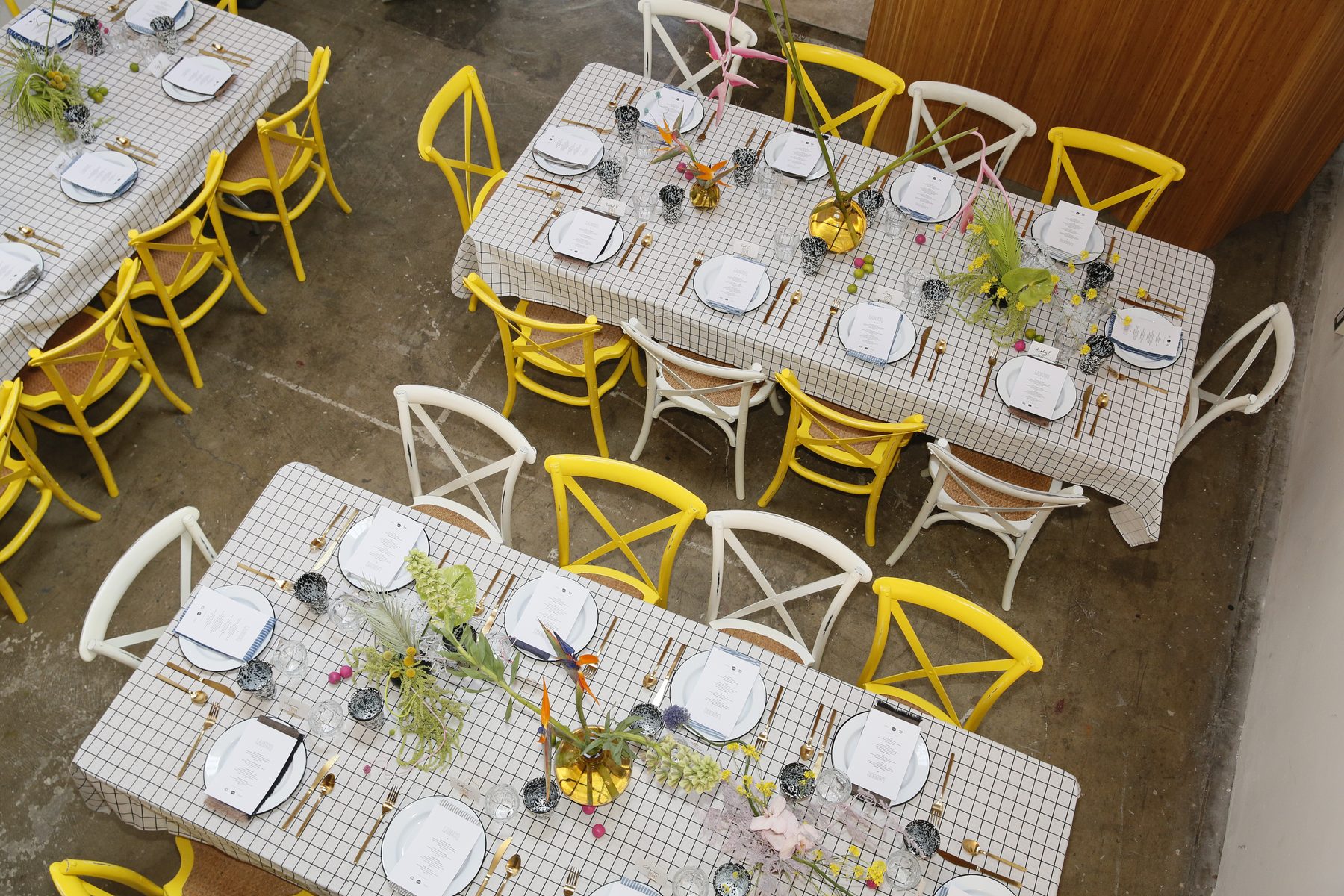 An overhead view of a long grid-cloth lunch table with yellow chairs