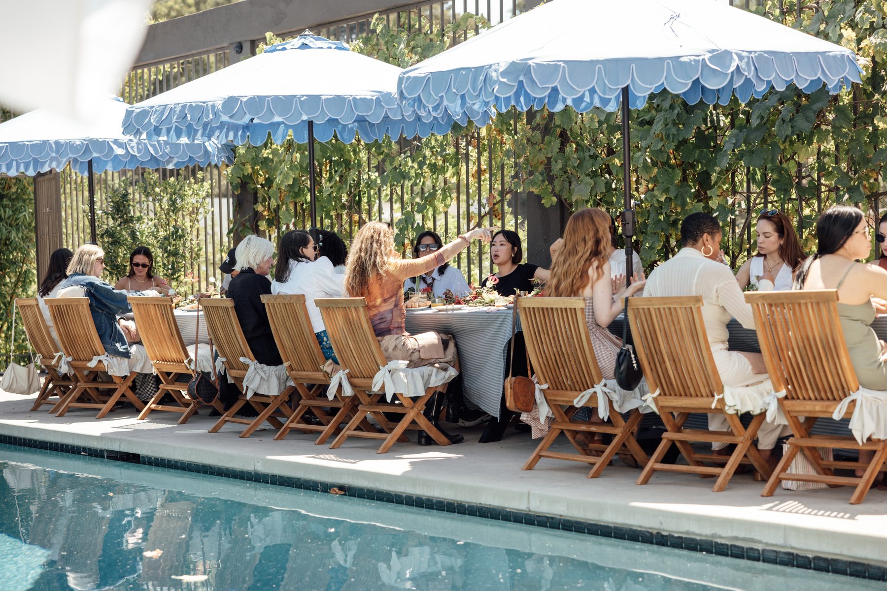A long poolside lunch under scalloped blue umbrellas against a vine wall