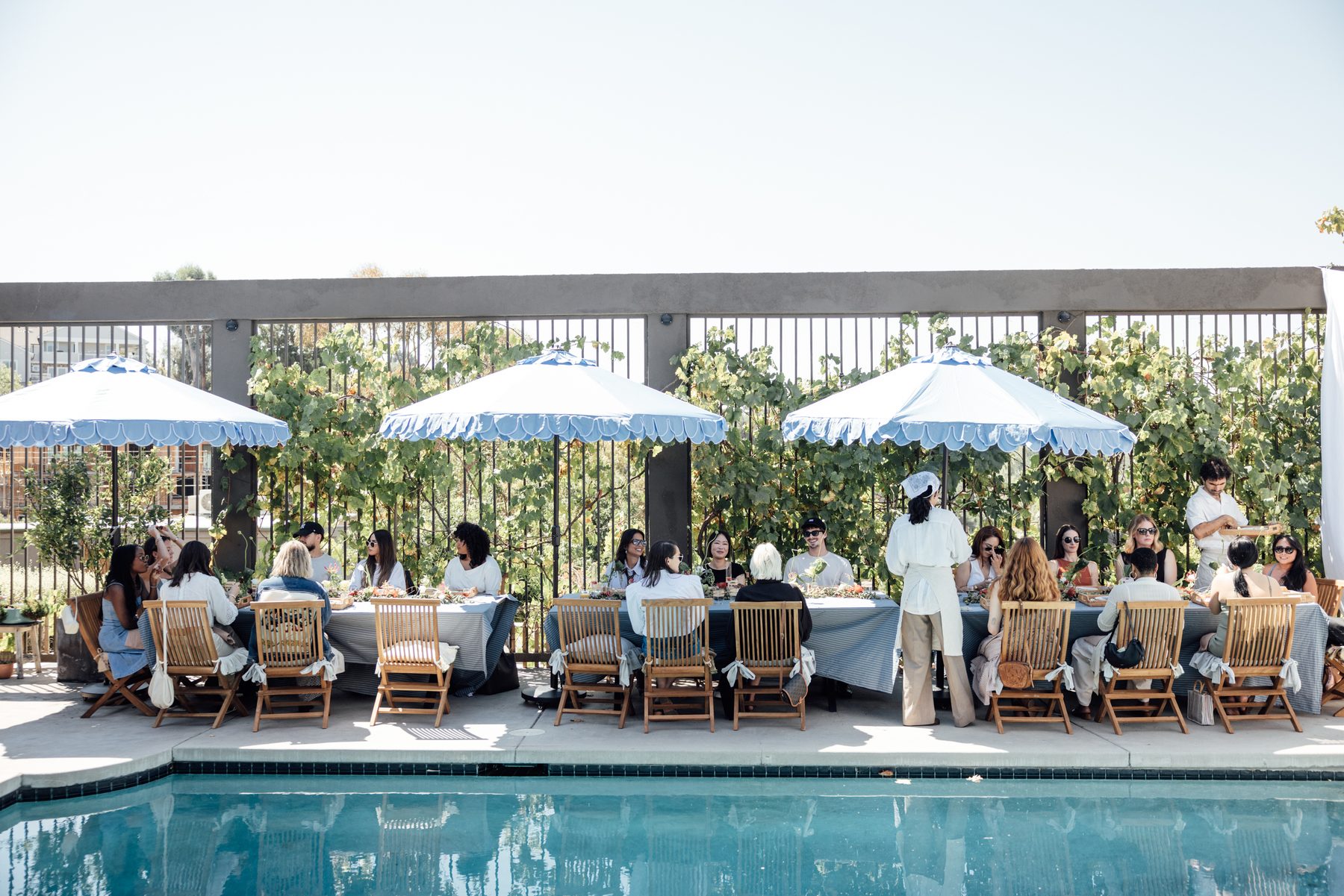 A long poolside table under scalloped umbrellas
