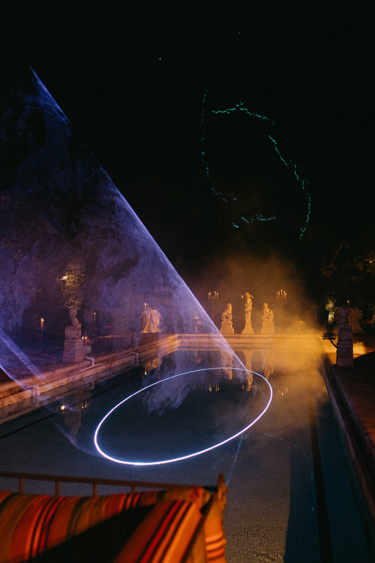A glowing light ring over the reflecting pool among marble statuary and candelabra