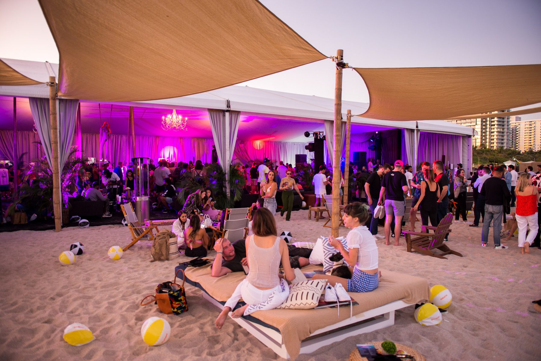 A DJ plays a crowded tent washed in magenta light