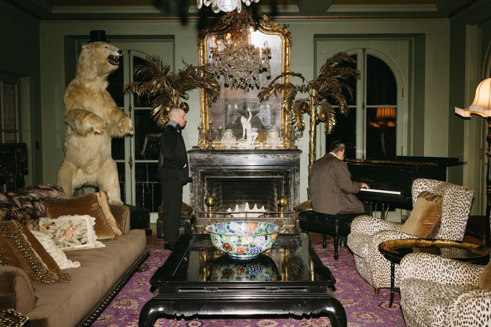 A pianist plays beside a standing polar bear mount in a green salon