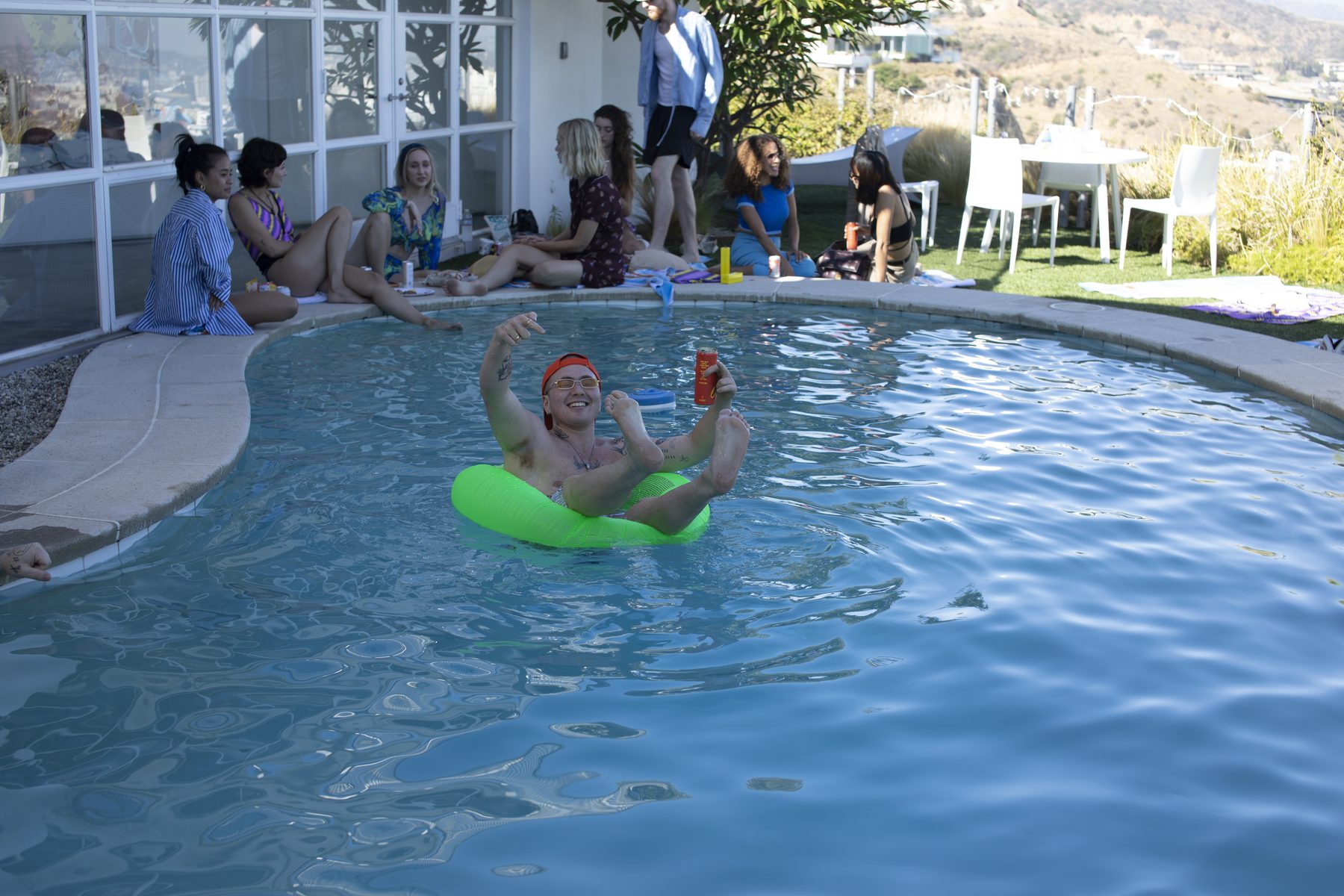 A guest floats in a pool at a hillside daytime party