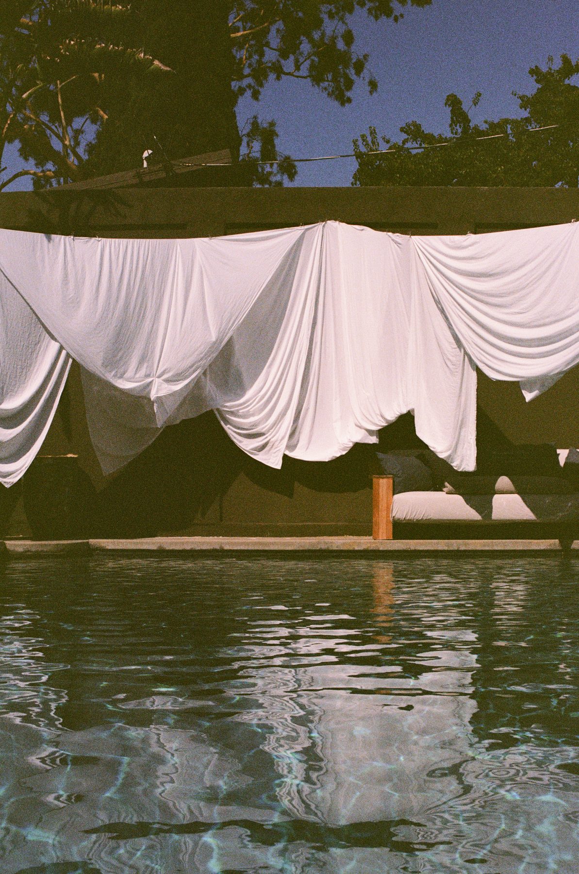White draped cabana fabric mirrored in a pool at dusk