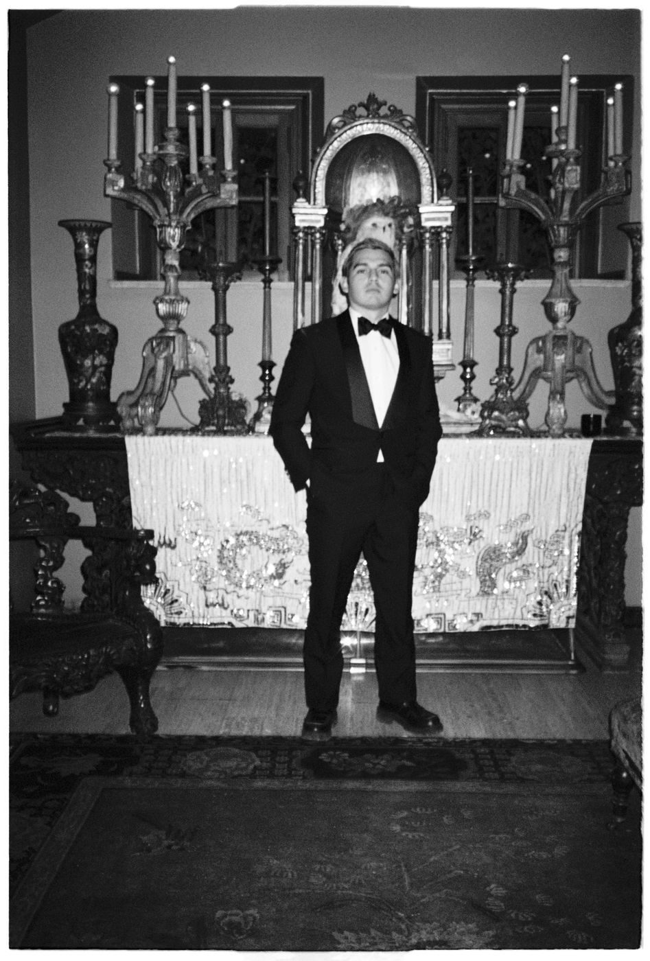 Black-and-white portrait of a guest in a tuxedo before a candelabra