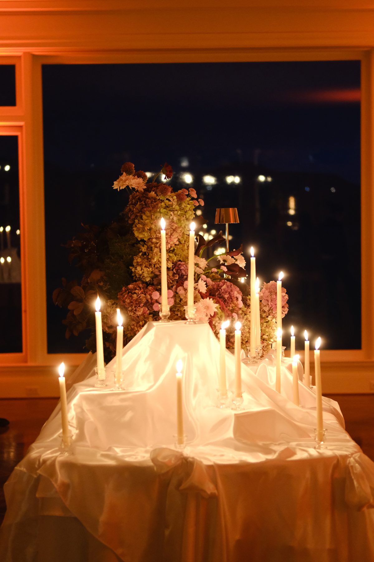 A candlelit table with dried florals before a window of bay lights