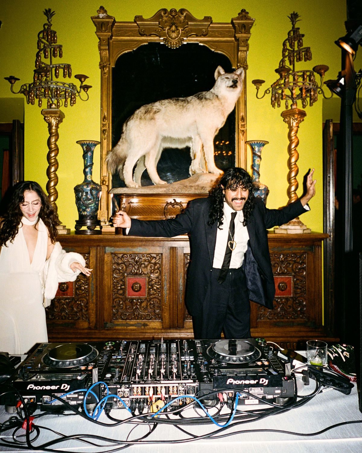 A DJ beneath a taxidermy wolf and gilded mirror